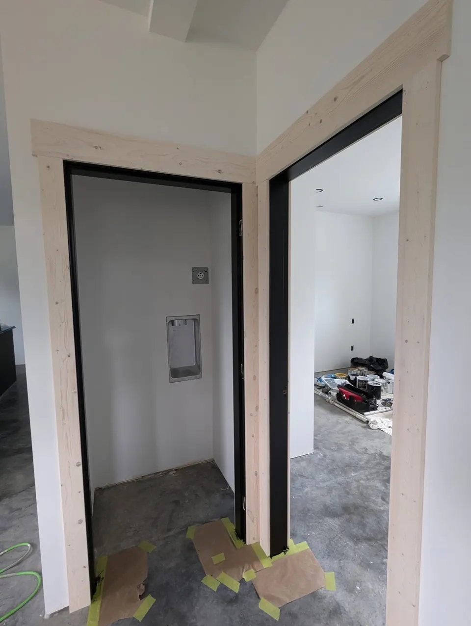 Two doorways with black jambs and natural wood casing on white walls